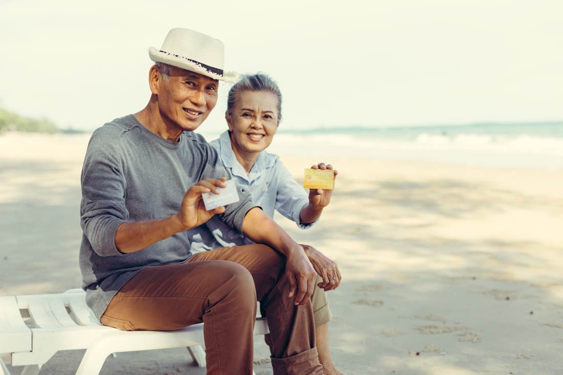 Retired Asian-Australian couple relaxing on a beach overseas, illustrating Australian expats living abroad in retirement