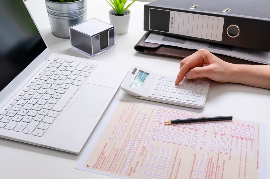 Person completing an Australian tax return at a desk with calculator, laptop and folders of rental property records