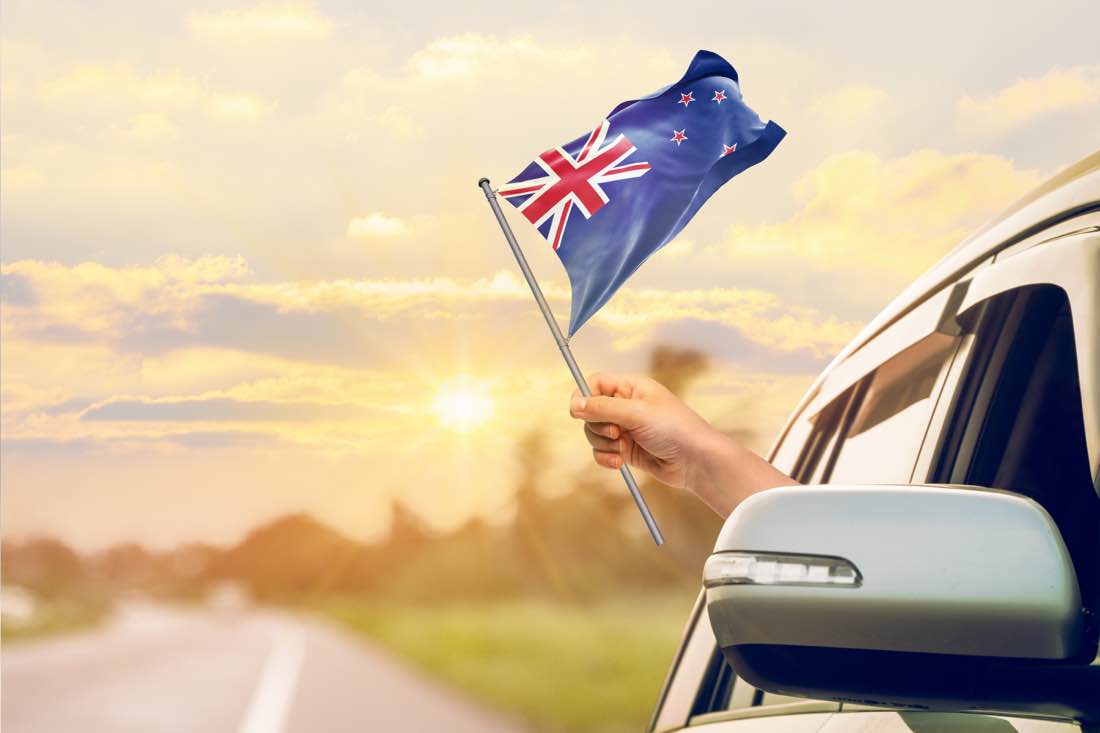 New Zealand flag held from a car window at sunset, representing Australian relocation to New Zealand after 2026 Budget CGT changes.